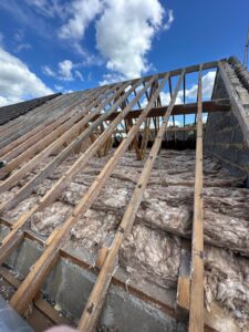 Exposed wooden roof rafters and existing loft insulation during roof renovation in Dorset