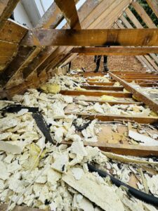 Broken old insulation debris and exposed wooden rafters during attic clearance in Gloucestershire
