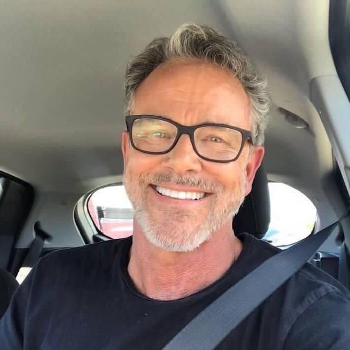 A smiling middle-aged male customer with glasses and grey hair, sitting in his car in Buckinghamshire, giving a positive review for Spray Foam Removal UK after a successful project.