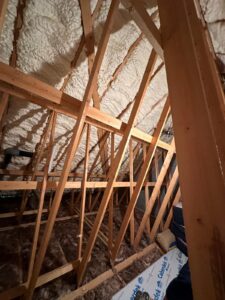 Spray foam insulation applied to roof rafters in loft space with exposed wooden beams in Bedfordshire