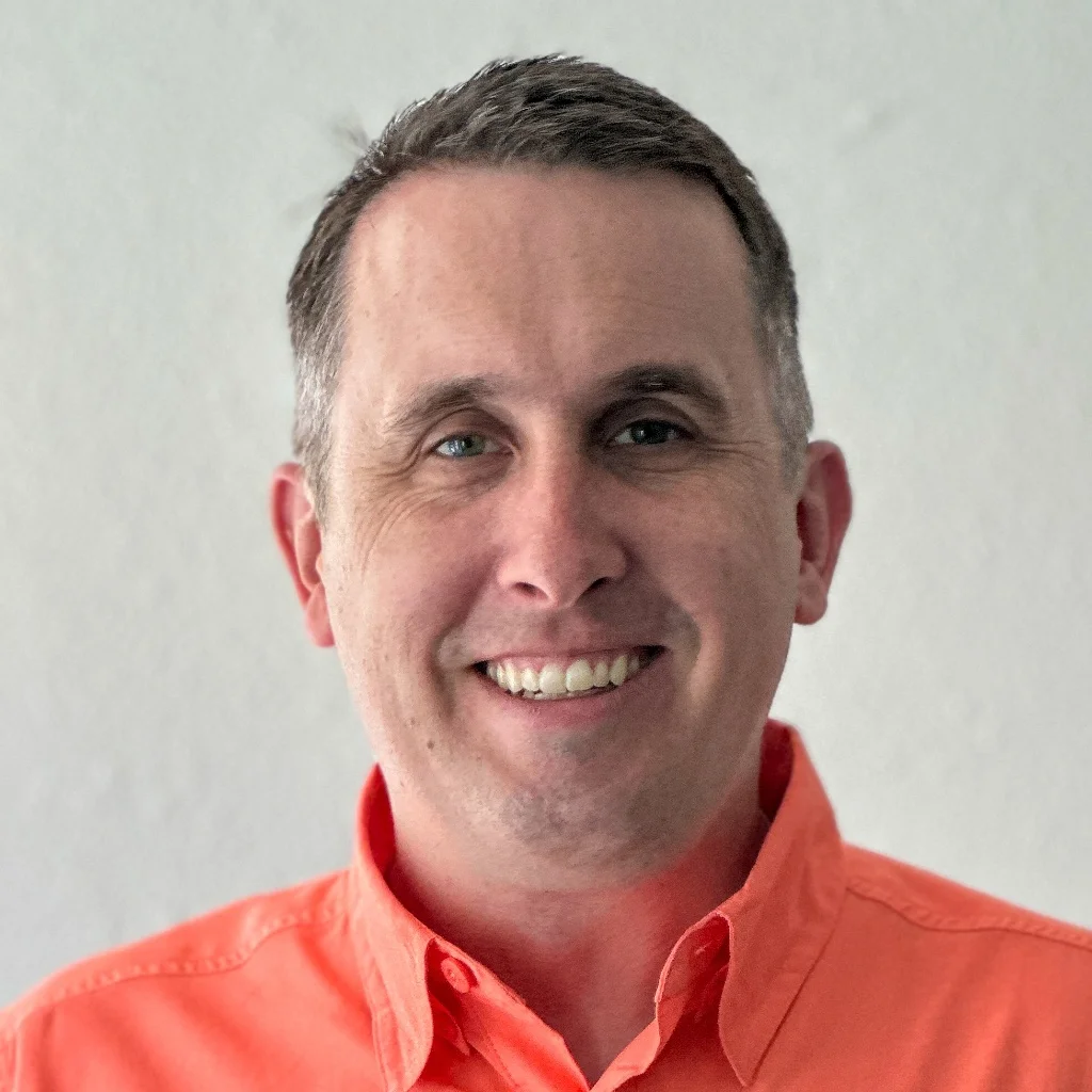 A headshot of a smiling middle-aged man in an orange button-down shirt, sharing his experience as a satisfied Spray Foam Removal UK client in Banbury, Oxfordshire