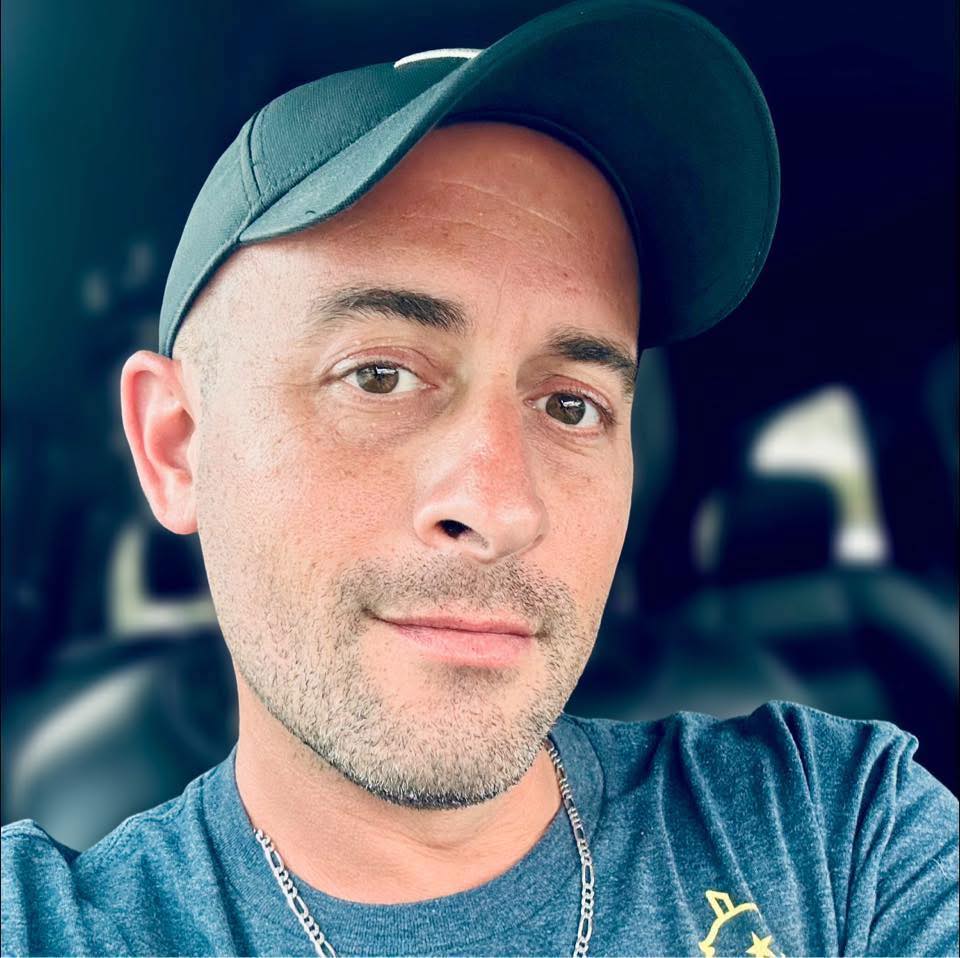 A close-up of a male customer wearing a green baseball cap and a dark blue tee, smiling in his car after receiving his spray foam removal certificate for his home in Daventr