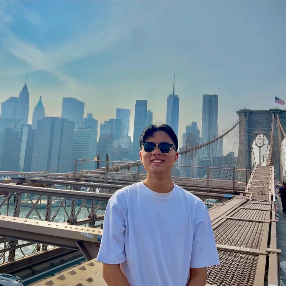 A smiling young man with sunglasses and a white t-shirt, standing on a bridge with a city skyline in the background. This image is used for a property service review for a resident in the Ironbridge and Telford area of Shropshire.