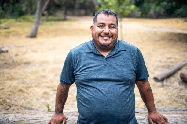 A smiling middle-aged man with short blonde hair, wearing a dark navy suit and a light green patterned tie. He represents a professional homeowner in Lancaster who successfully resolved mortgage survey issues through spray foam extraction.
