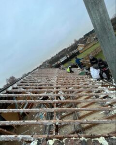 Roofing crew working on exposed wooden roof battens during stripping and renovation in Norfolk