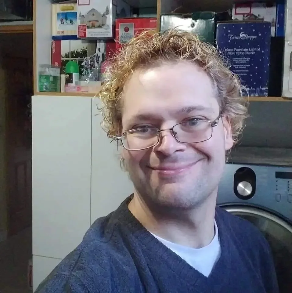 A portrait of a smiling middle-aged man with short brown hair, standing outdoors in front of a grand stone building in Leeds. This image is used as a customer testimonial for successful spray foam insulation removal.