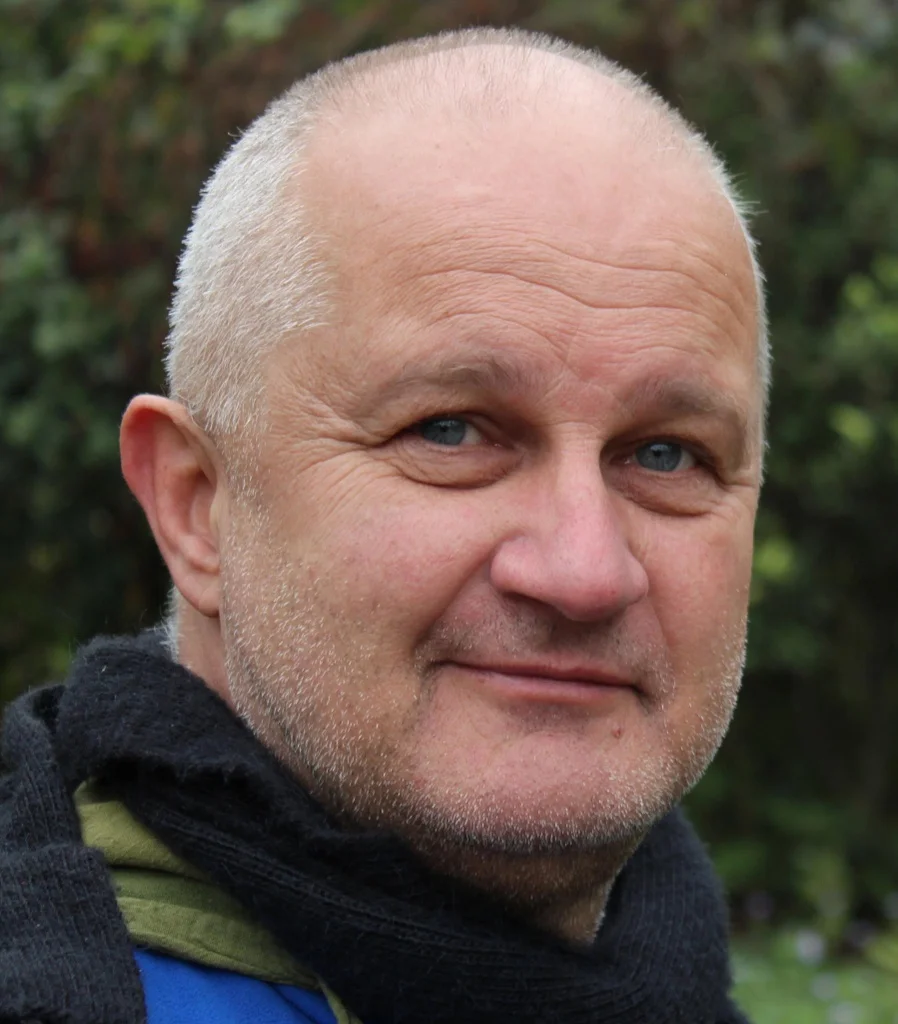 Portrait of a smiling senior man with a bald head and light stubble, wearing a black scarf and blue jacket, providing a local testimonial for spray foam removal services in Leominster.