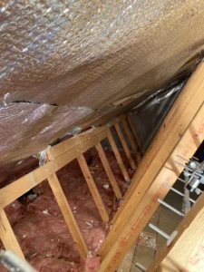 Pink fiberglass insulation between wooden rafters with foil-backed membrane in Lancashire loft renovation