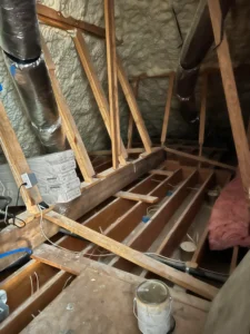 Wooden floor joists being installed in loft space with spray foam insulation and ventilation ducts in Merseyside