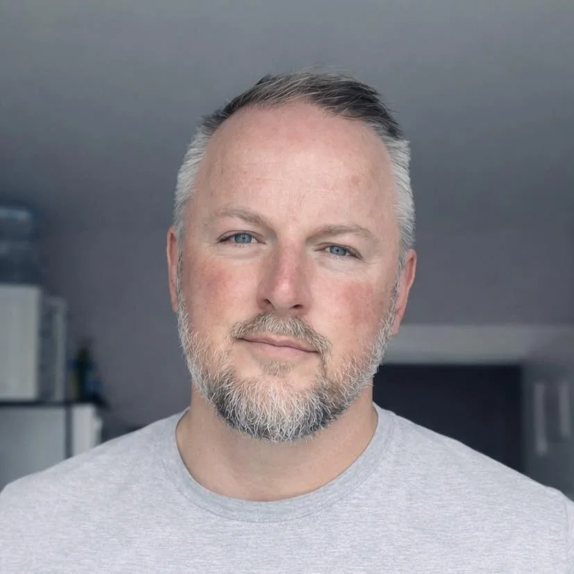 Close-up portrait of a middle-aged man with short grey hair and a full grey beard, wearing a light grey t-shirt, used as a local customer testimonial in March, Cambridgeshire.