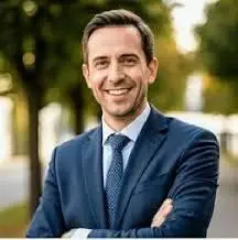 A professional man in a blue suit with his arms crossed, smiling. This visual is used for a testimonial on a Preston residential property landing page, focusing on professional loft timber auditing after insulation removal.