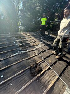 Roofing crew standing on exposed wooden battens and old timber decking during roof stripping in Cornwall
