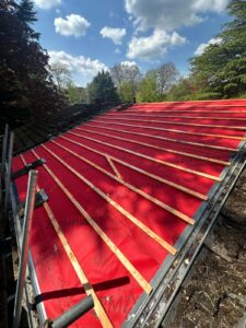 Bright red breathable roof membrane with wooden battens installed on a residential roof in Worcestershire under a blue sky