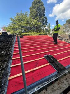 Roofing contractor standing on red breathable membrane and timber battens during roof renovation in the West Midlands
