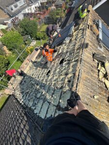 POV shot of roofing contractors stripping old tiles and clearing debris from a pitched roof in East Sussex