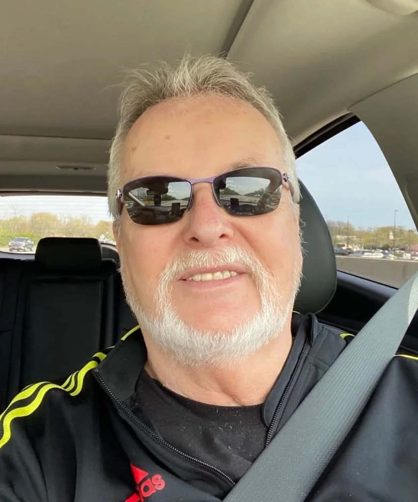 Outdoor portrait of a smiling middle-aged man with white hair and a beard, wearing sunglasses and a black Adidas jacket, used as a customer testimonial for spray foam removal in Rugby, Warwickshire.