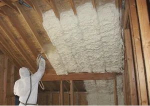 Professional installer in protective gear actively spraying white foam insulation between wooden roof rafters in a Northumberland loft