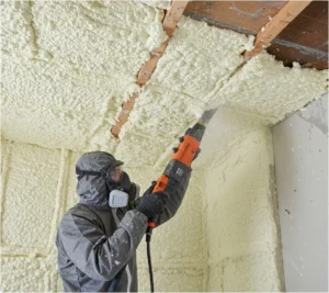 Professional installer in protective gear trimming yellow spray foam insulation with a power saw in a South Yorkshire loft