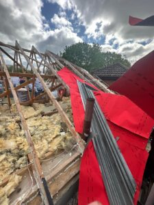 Wooden roof trusses with yellow insulation and red breathable membrane during roof renovation in Hampshire