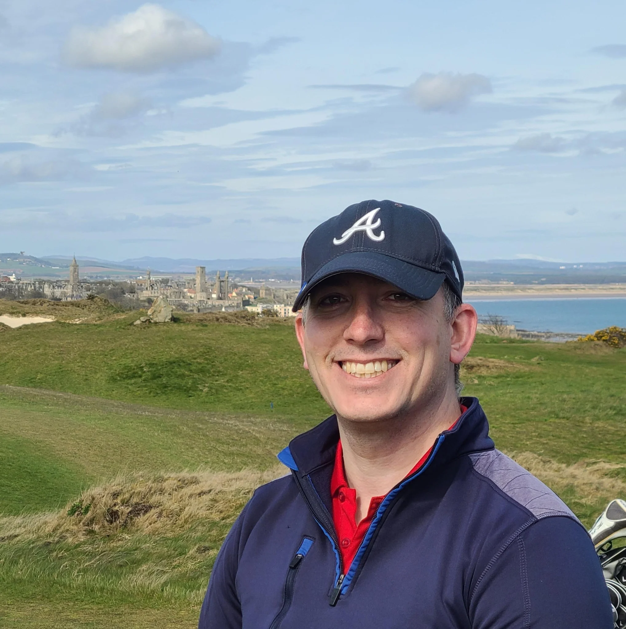 A cheerful local customer wearing a navy blue 'A' cap and a fleece jacket, standing outdoors on a golf course in Wiltshire after a successful loft insulation removal project by Spray Foam Removal UK.