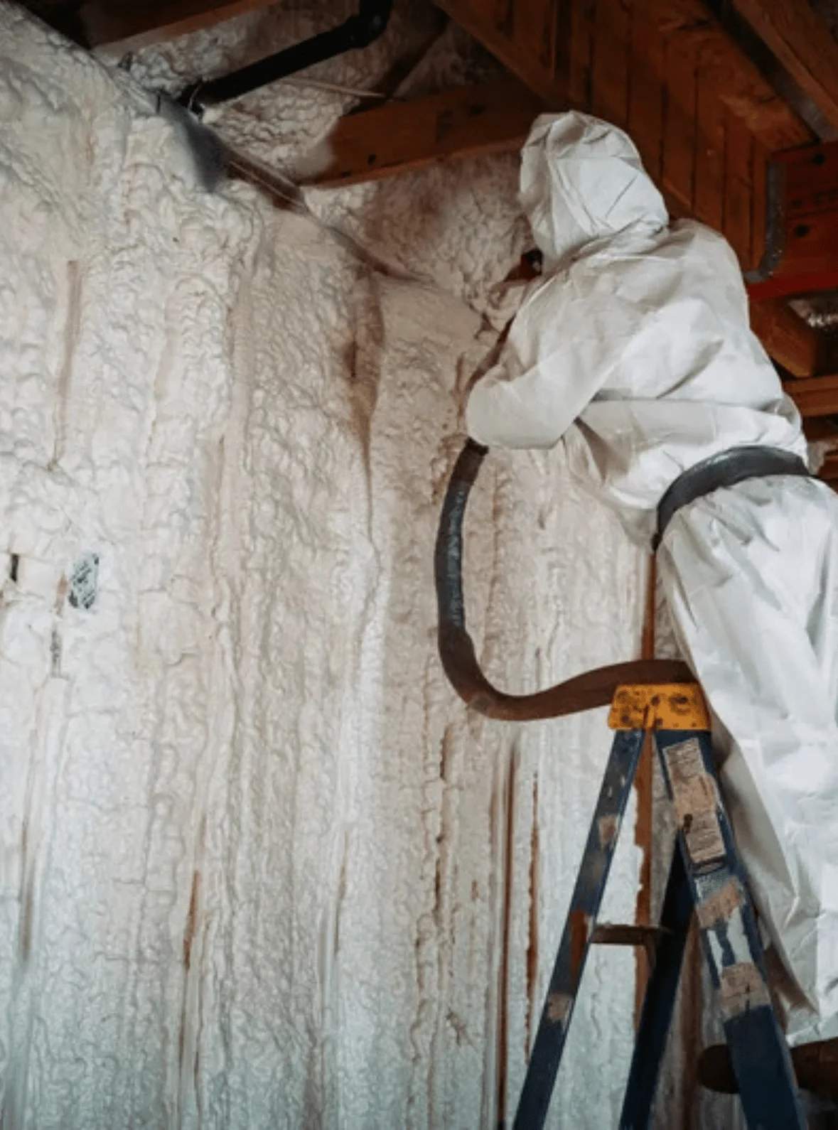 Professional installer in protective suit applying spray foam insulation to wall and ceiling joists in Portsmouth - expert home insulation services
