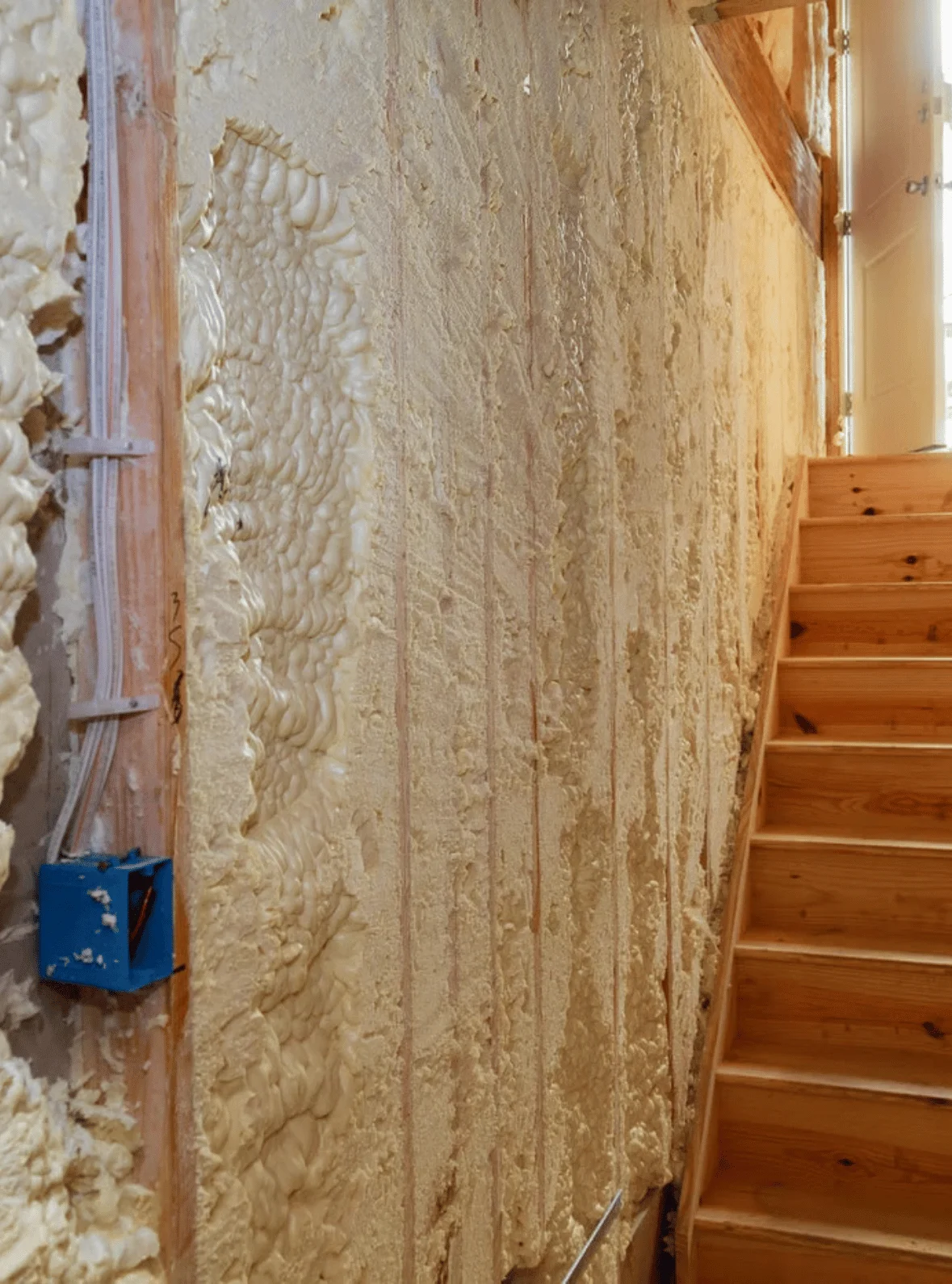 Professional spray foam insulation installation in wall cavity near staircase - Portsmouth insulation contractors providing energy-efficient home insulation services