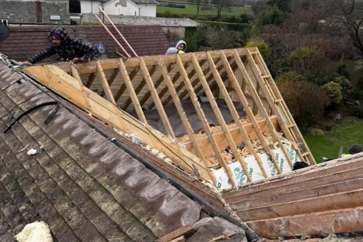 Spray foam insulation removal and roof restoration in Rutland, contractors removing old tiles and insulation from timber rafters with countryside view