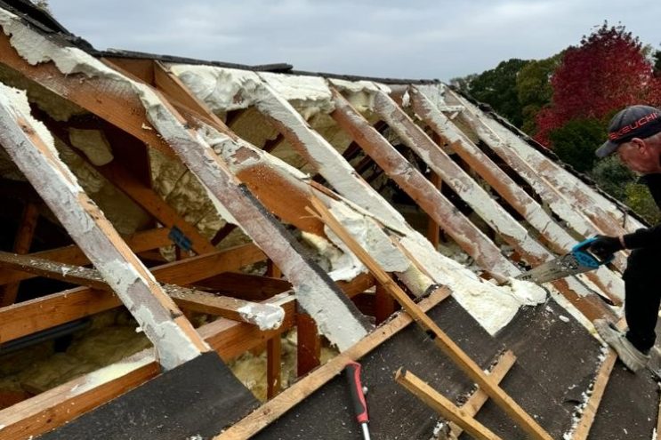 Professional spray foam removal in Essex, contractor cutting away old foam insulation from roof beams to restore timber