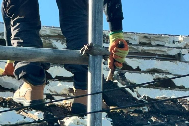 Roofer removing old tiles and insulation during roof repair project in Bedfordshire, professional roofing contractor on scaffolding