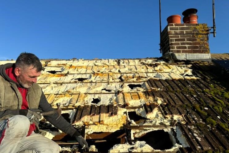 Roofer removing spray foam insulation from timber rafters in Herefordshire, showing damaged roof structure and extraction process