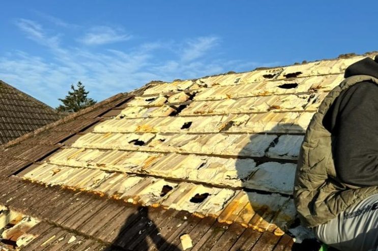 Roofer removing spray foam insulation from roof in Hertfordshire, showing exposed timber rafters and tile removal during insulation extraction